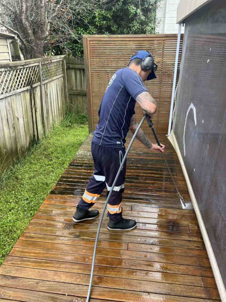 A Suds Wash Co specialist pressure washing a wooden deck in Auckland, carefully removing built-up mould and dirt to restore the timber’s natural colour.