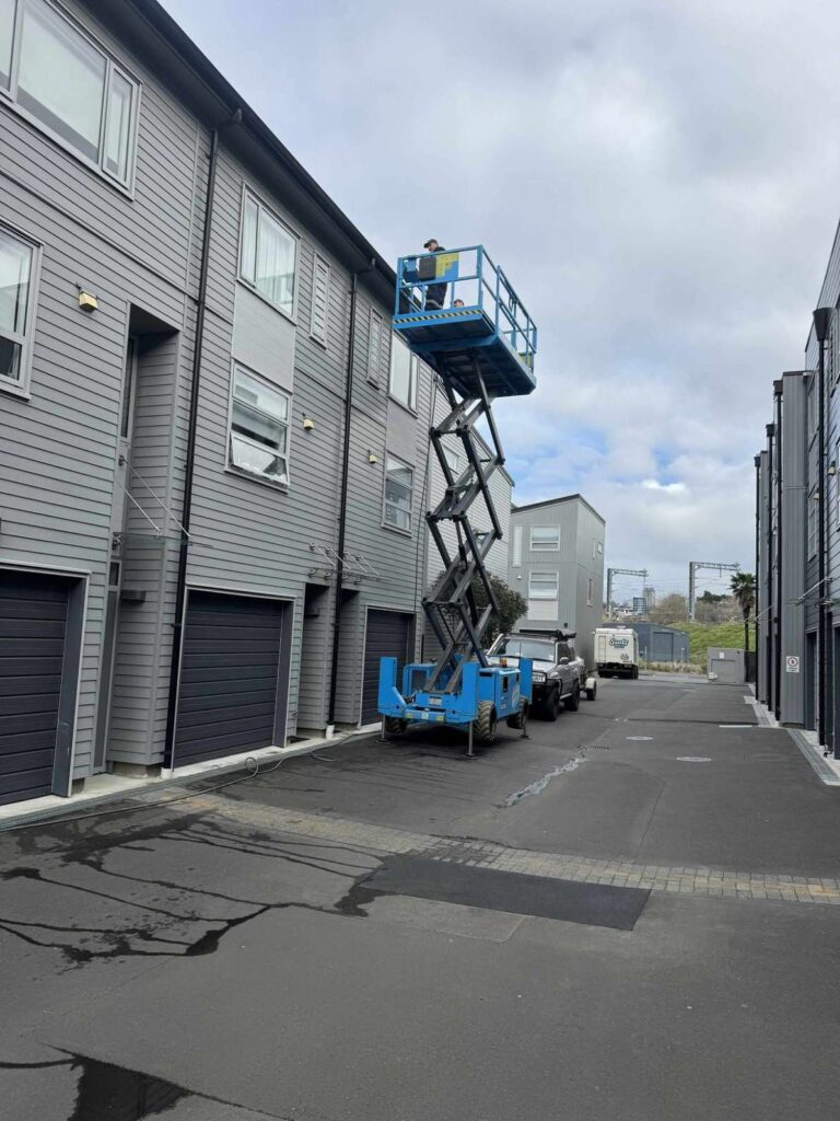 Exterior cleaner using a scissor lift to wash a low-rise Auckland apartment complex.